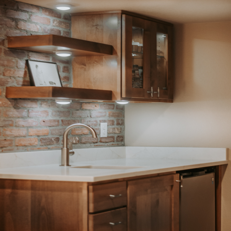 Basement wet bar with wood cabinetry and floating shelves in Northern Colorado by Blue Springs Construction
