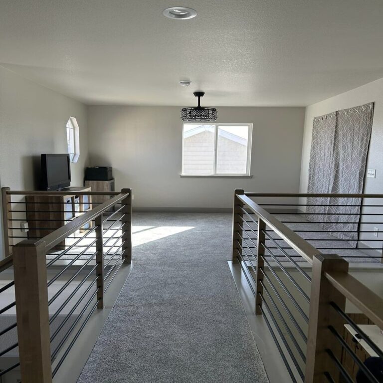 Upper landing with a horizontal metal railing overlooking the living space